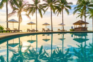 Four sets of pool chairs under umbrellas surrounding a luxury hotel pool in a tropical setting.