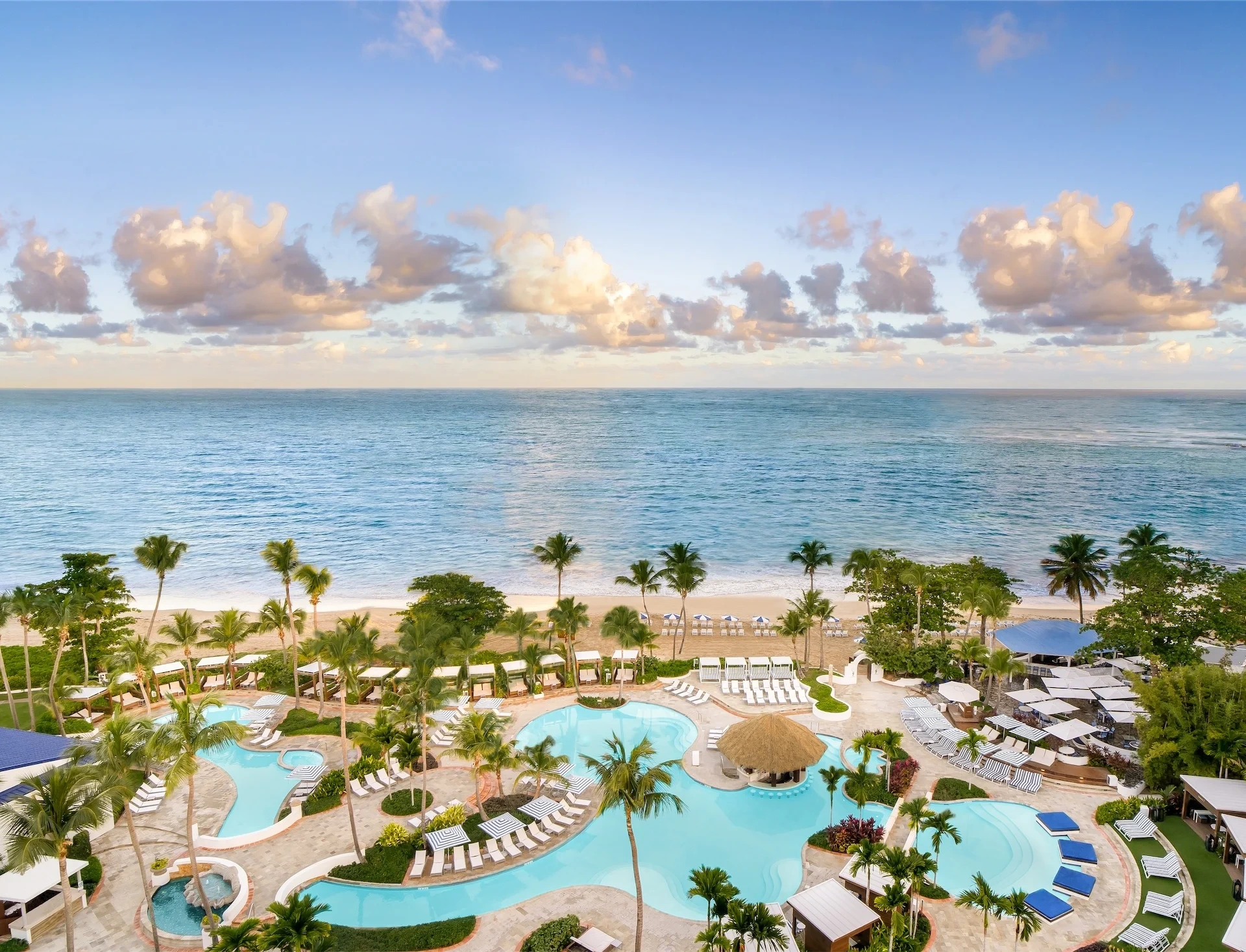 Aerial view of pools, palm trees, beach, and ocean at Fairmont El San Juan Hotel.