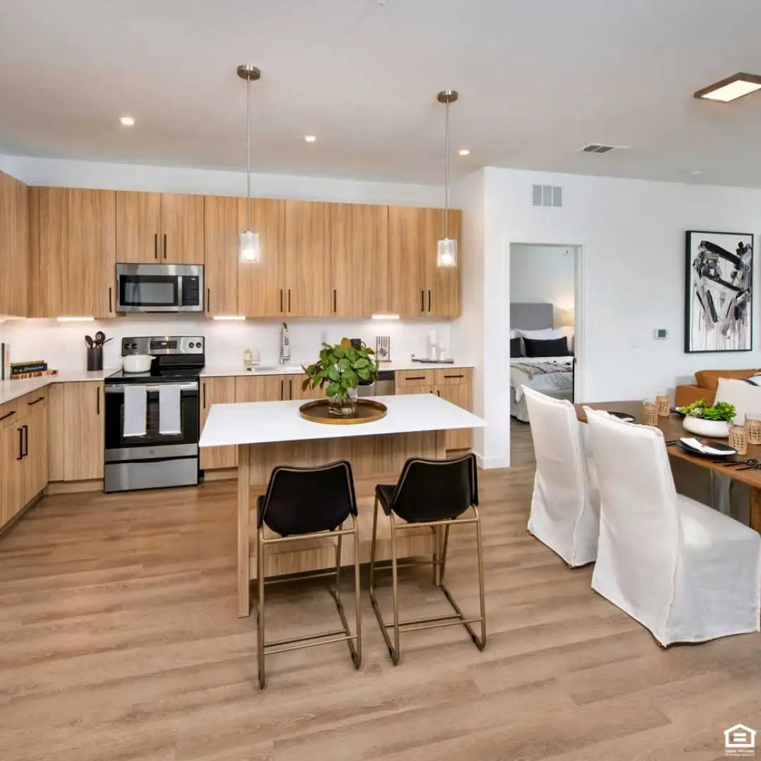 Cypress Manor apartment kitchen with wood cabinets, two black counter stools, and an adjoining dining area with white chairs.
