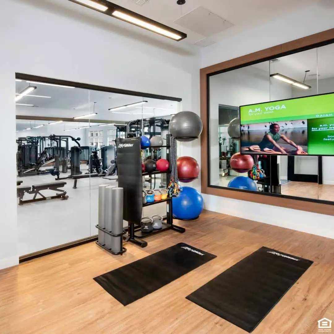 Cypress Manor fitness room with exercise mats, kettlebells, stability balls, mirrored walls, and a television.