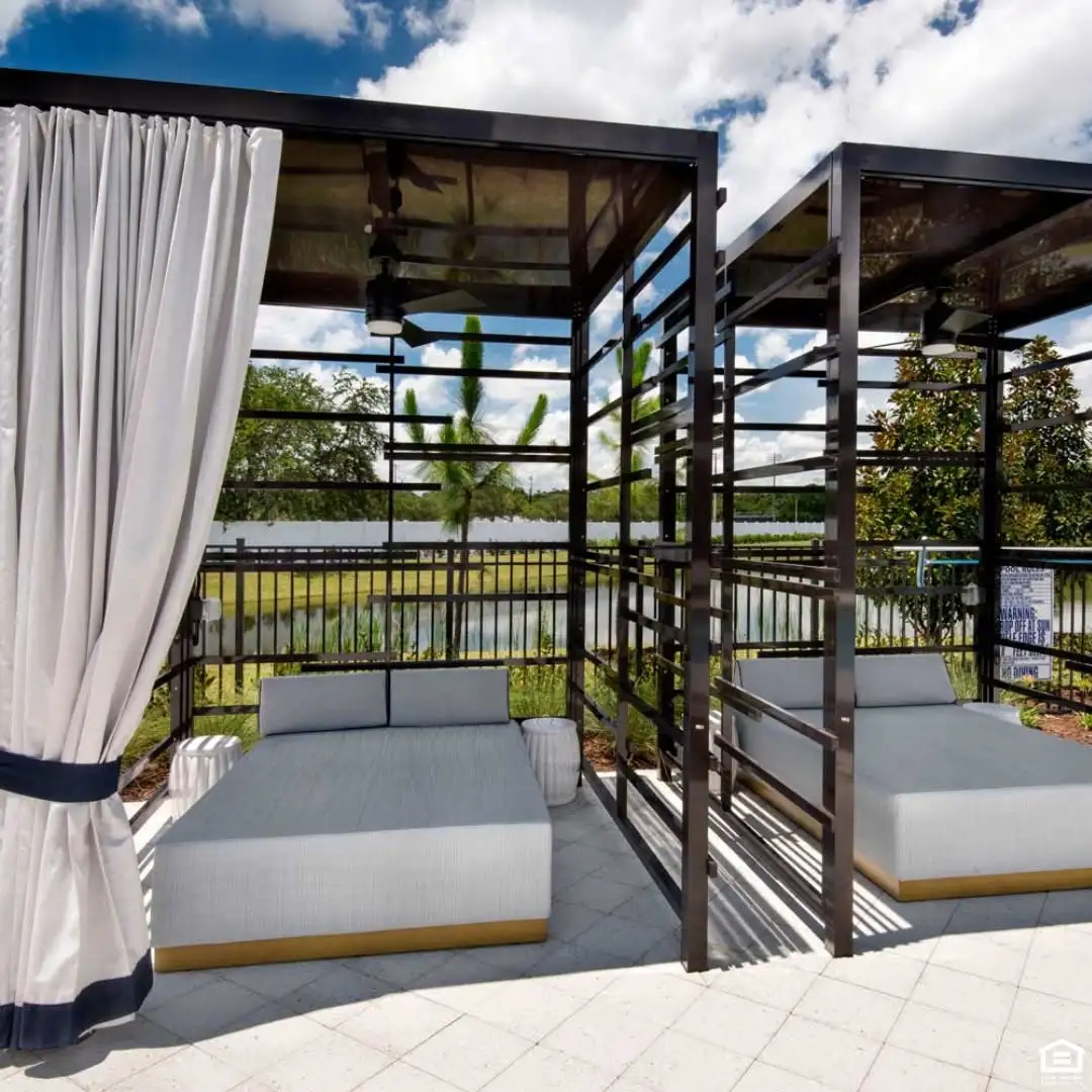 Cypress Manor outdoor cabanas with cushioned daybeds, white curtains, and small side tables overlooking a pond.