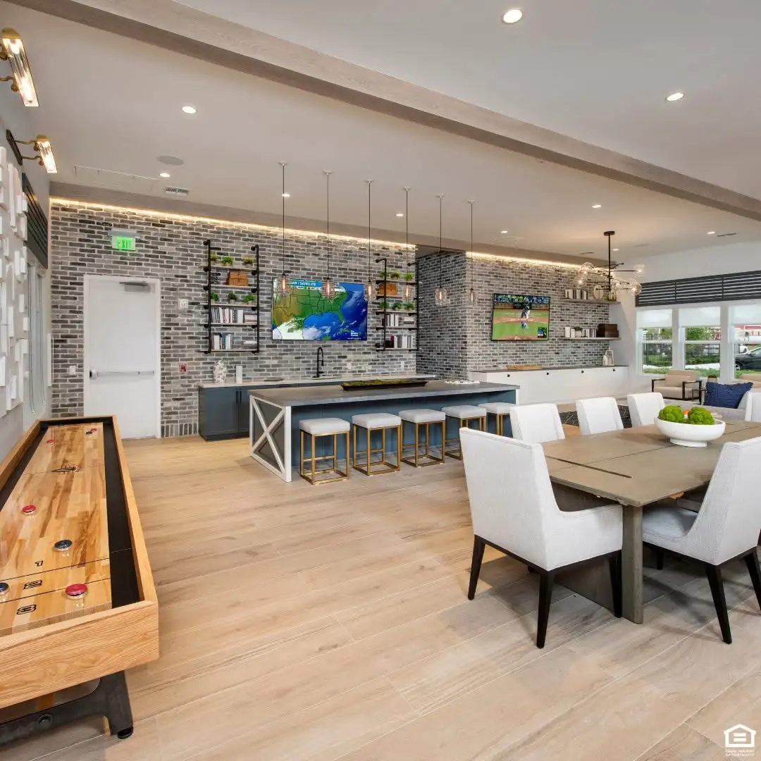 Cypress Manor shared lounge with a dining table, upholstered chairs, counter stools, wall mounted televisions, and a shuffleboard table.